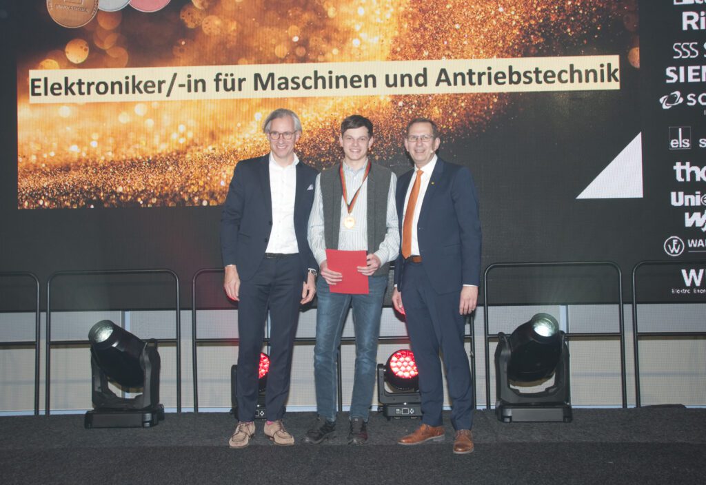 Johannes Lang, Auszubildender bei VINCORION, in der Produktion in Altenstadt. Foto: VINCORIONJohannes Lang (Mitte) mit DMH-Schirmherr Dr. Philipp Dehn (links) und ZVEH-Vizepräsident Karsten Krügener (rechts) in Oldenburg. Foto: VINCORION